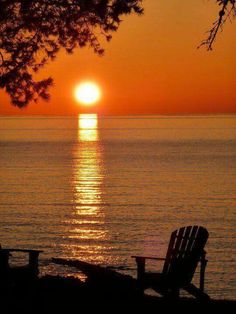 the sun is setting over the ocean with two chairs