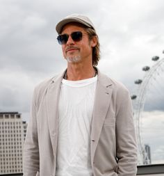 a man wearing sunglasses and a hat standing in front of a ferris wheel with his hands in his pockets