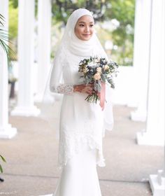 a woman in a white wedding dress holding a bouquet and wearing a hijab