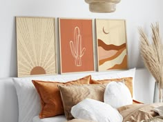 three prints on the wall above a bed in a room with pillows, blankets and throw pillows