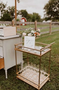 a small bar cart with wine glasses on it and flowers in vases next to it