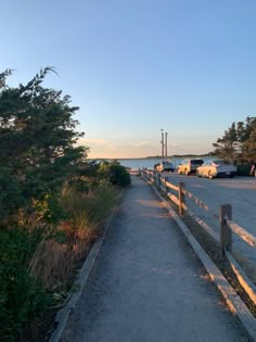 there are cars parked on the side of the road next to the water and trees