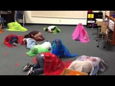 several children are laying on the floor covered in plastic bags and covering them with colorful cloths