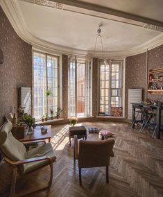 a living room filled with lots of furniture next to two large windows and wooden floors