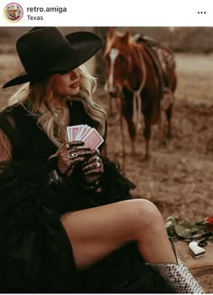 a woman sitting on the ground next to a horse and holding a deck of cards