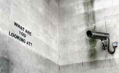 a security camera on the side of a building with graffiti written on it that says, what are you looking at?