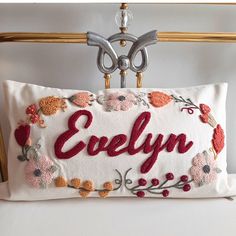 an embroidered pillow with the word evelyn on it hanging from a metal hanger in front of a white wall