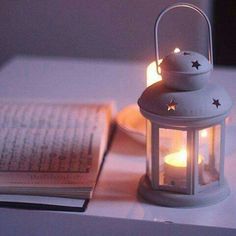 an open book on a table next to a white lantern with stars and light inside