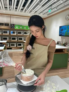 a woman in an apron decorating a cake with white frosting on a table