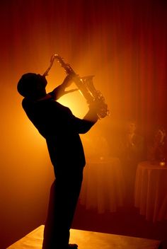 a man playing the saxophone in front of a red light