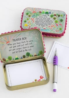 two tins with writing on them next to a pen and paper in the box