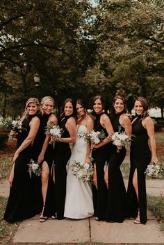 a group of women standing next to each other wearing black dresses and holding bouquets