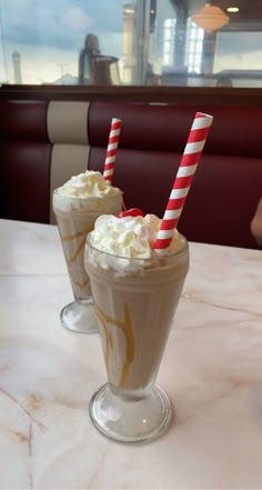 two drinks with whipped cream and candy canes on a table in a restaurant or cafe