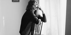 a black and white photo of a woman leaning against a wall talking on the phone