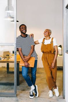 a man and woman standing in an office doorway smiling at each other while holding papers