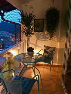 two chairs and a table on a balcony with plants in the background at night time