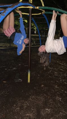 two children are playing on the swings in the park at night, one is upside down