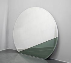 a round mirror sitting on top of a white floor next to a green vase and wall