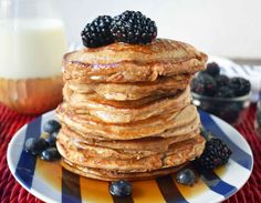 a stack of pancakes topped with berries and syrup on a plate next to a glass of milk