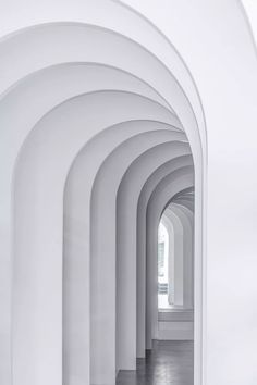 an arched hallway with white walls and wood flooring is seen in this image, there are many arches on the wall