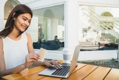 a woman sitting at a table with a laptop computer and holding a cup of coffee