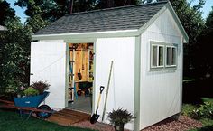 a white shed with a blue wheelbarrow and tools in the yard next to it