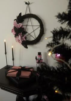 a black table topped with pink presents under a pentagram and candle holder next to a christmas tree