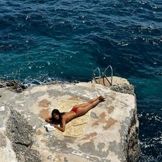 a woman laying on top of a rock next to the ocean