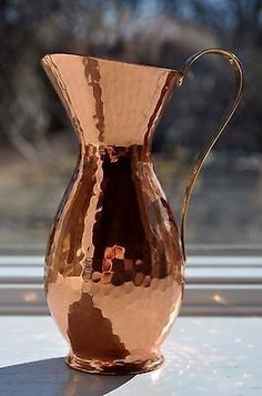 a copper colored pitcher sitting on top of a table next to a window sill