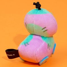 two pink and green stuffed animals sitting on top of an orange background with a black tag