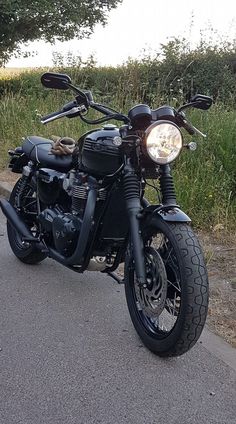 the motorcycle is parked on the side of the road next to some grass and trees