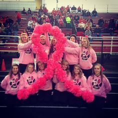 a group of girls in pink shirts holding up a heart shaped object at a sporting event