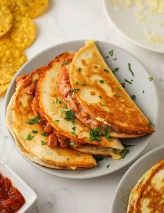 three quesadillas on plates with salsa and tortillas in the background