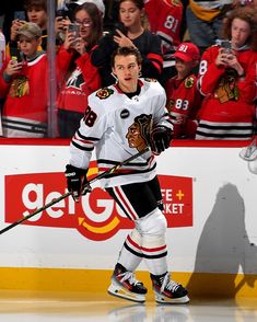 a hockey player is walking on the ice with his stick in hand and fans behind him