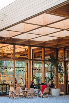 people sitting at tables in front of a building with lots of glass doors and windows