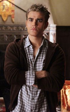 the young man is wearing a jacket and standing in front of a fireplace with his arms crossed