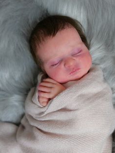 a baby wrapped in a blanket sleeping on top of a fur covered floor with his eyes closed