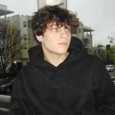 a young man with curly hair wearing a black hoodie and looking off into the distance