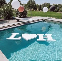 a pool with balloons floating around it and the word love spelled out in the water