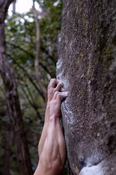 a person climbing up the side of a large rock with their hand on it's face