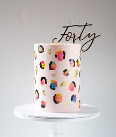 a white cake with colorful flowers on it and the word forty spelled in gold letters