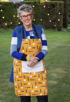 an older woman with glasses is standing in the grass and smiling at the camera while wearing an apron