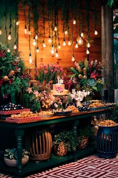 a buffet table filled with lots of food and flowers on it's sides, surrounded by hanging lights