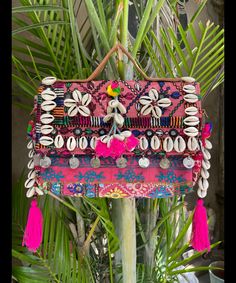 a pink purse with shells and tassels hanging on a palm tree in front of a house