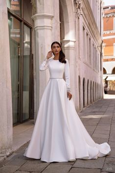 a woman in a white wedding dress standing on the sidewalk with her hands behind her head