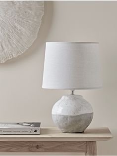 a white lamp sitting on top of a wooden table next to a book and magazine