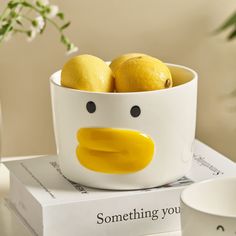 a bowl with lemons in it sitting on top of a book next to a cup