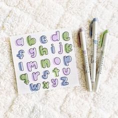 three markers and two pens on a sheet of paper with the letters drawn in it