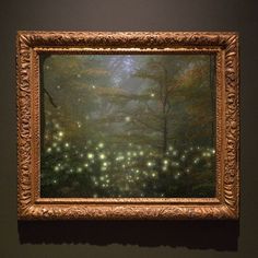 a painting hanging on the wall in front of a dark background with fireflies flying over it