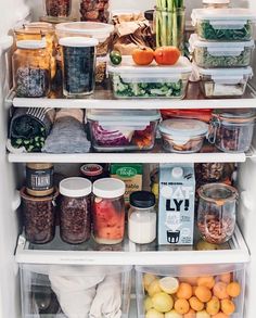 an open refrigerator filled with lots of food and containers full of fruit, vegetables, and other items